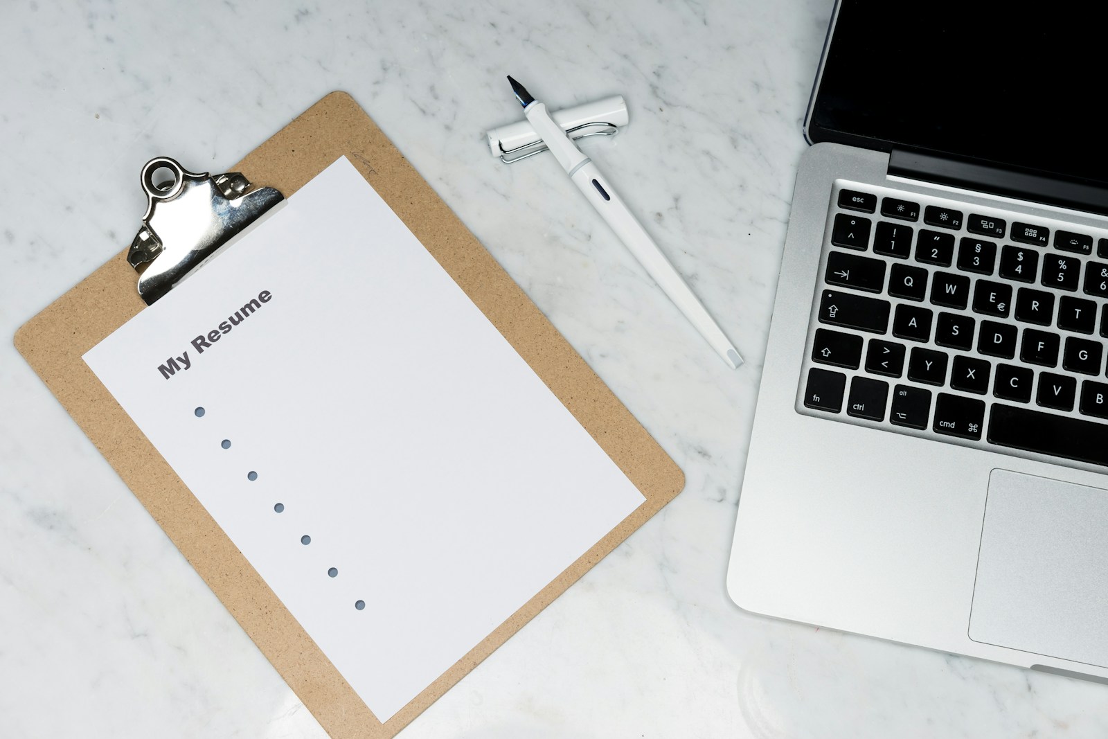 Printed resume and hands next to an open laptop on a desk.